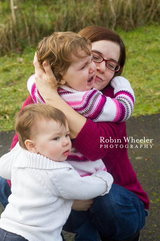 Mother comforting crying toddler and baby sister trying to comforter her, too, Dallas, Oregon