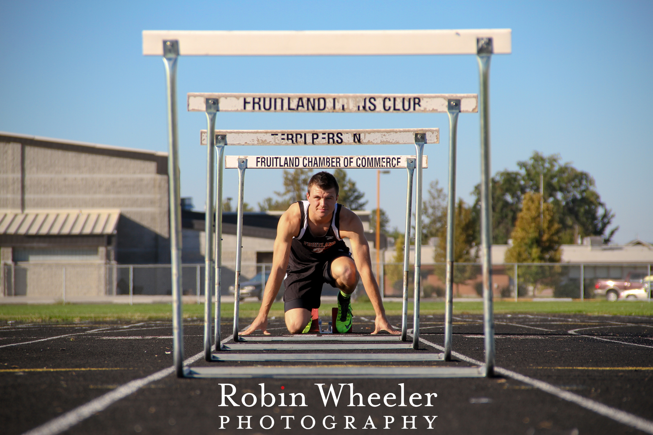 High school senior boy in starting blocks, as seen through a line of hurdles