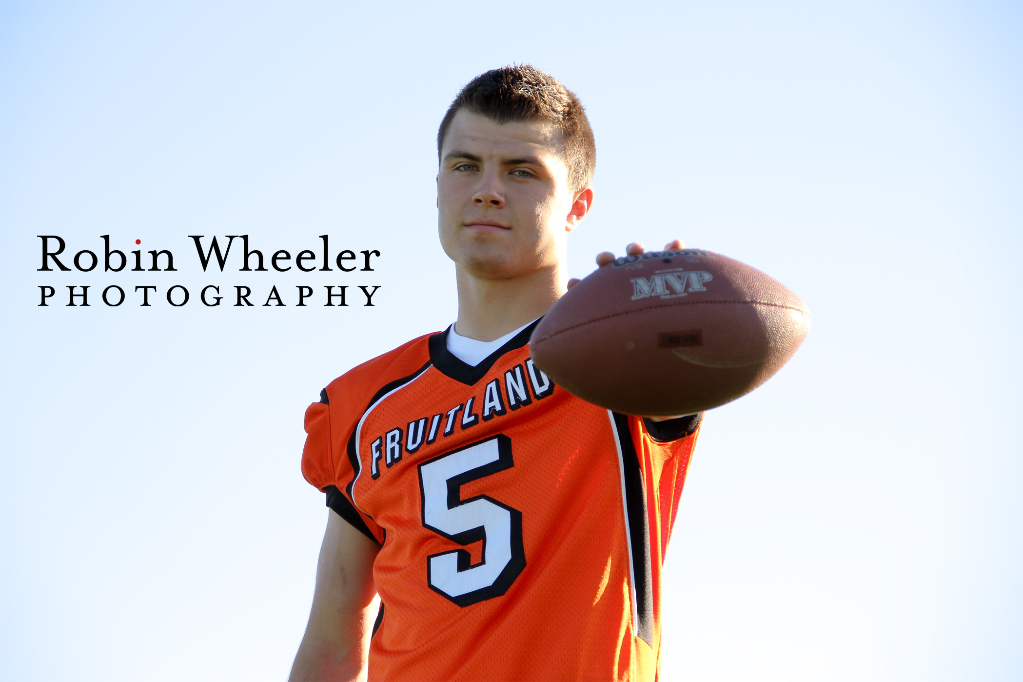 High school senior in football jersey holds football out in front