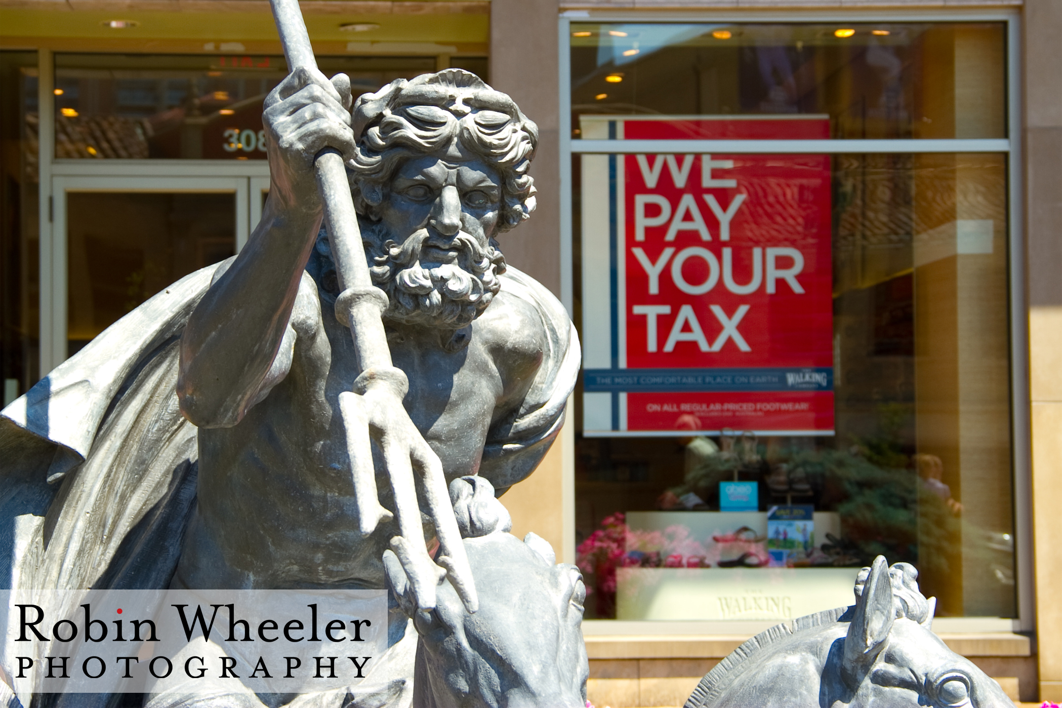 "We Pay Your Taxes Sign" behind sculpture of Neptune with trident