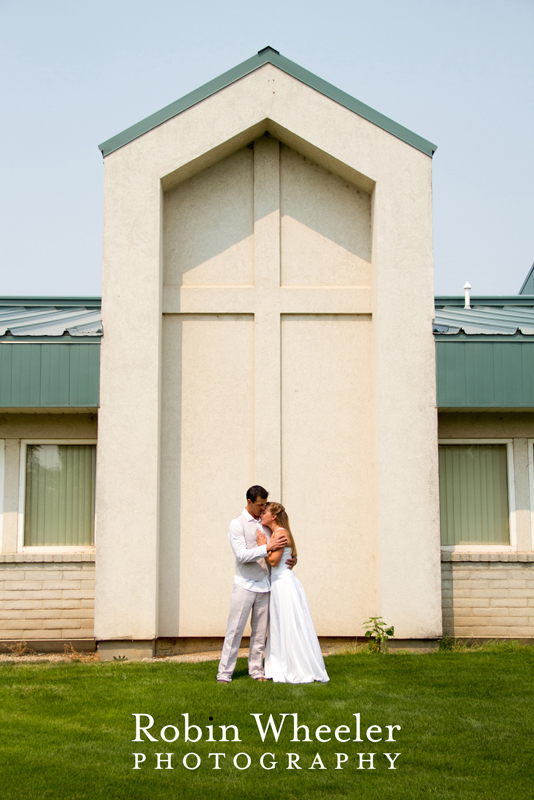 Portrait of bride and groom standing in front of a large cross in the side of a church, Ontario, Oregon