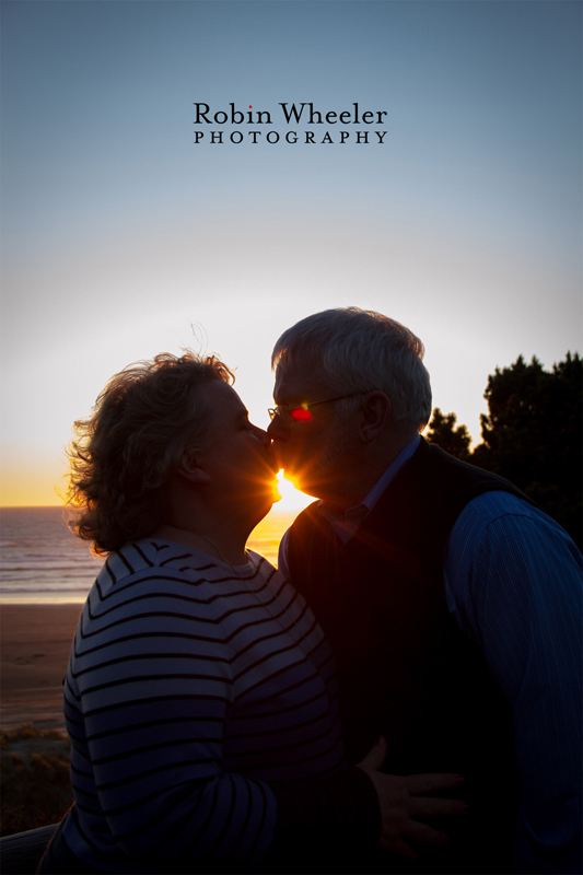 Portrait of a couple kissing at sunset with the ocean and sun behind them, Newport, Oregon