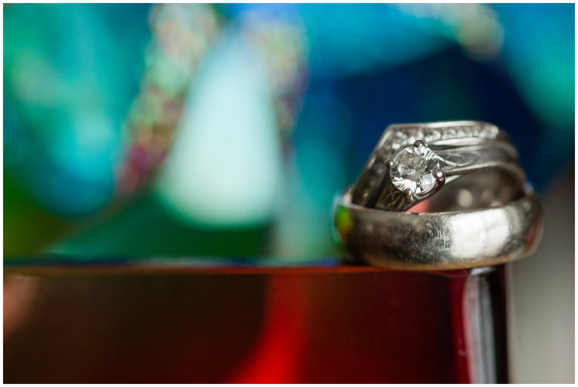 Wedding rings on the edge of a red vase with a pinwheel in the background