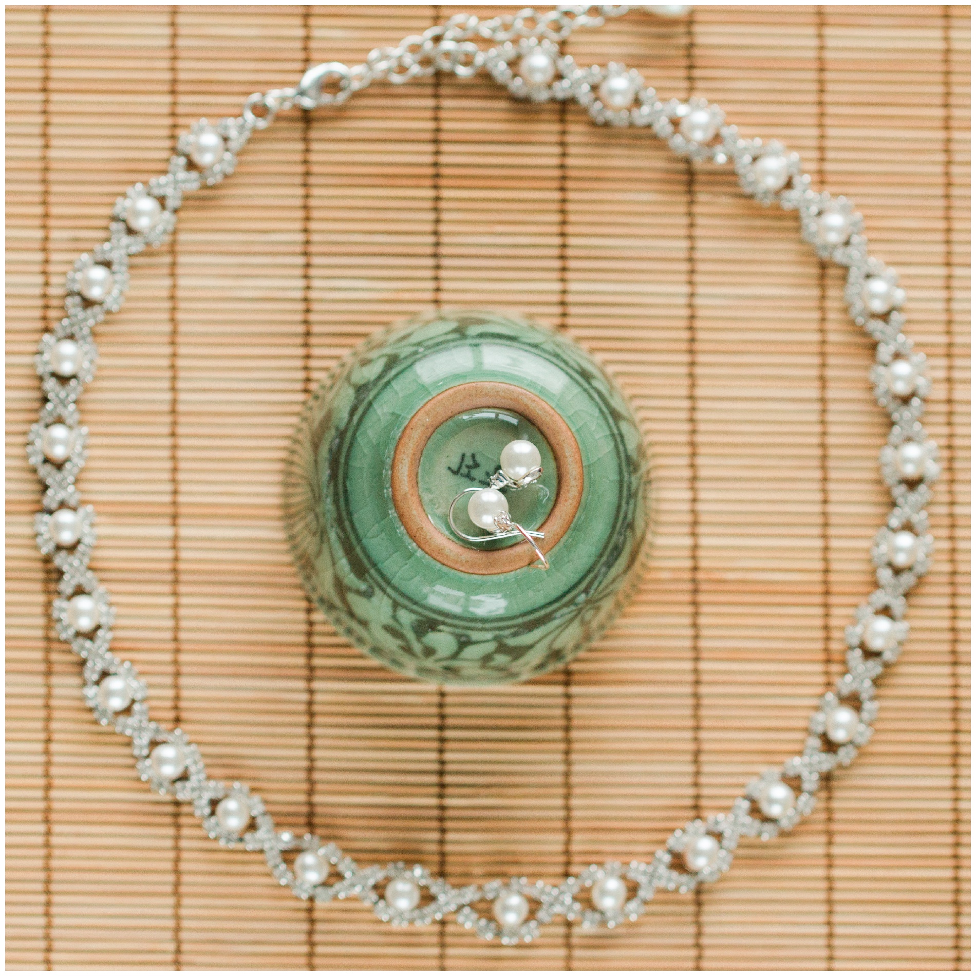 Pearl and diamond fishhook earrings and necklace on a bamboo mat with a teacup