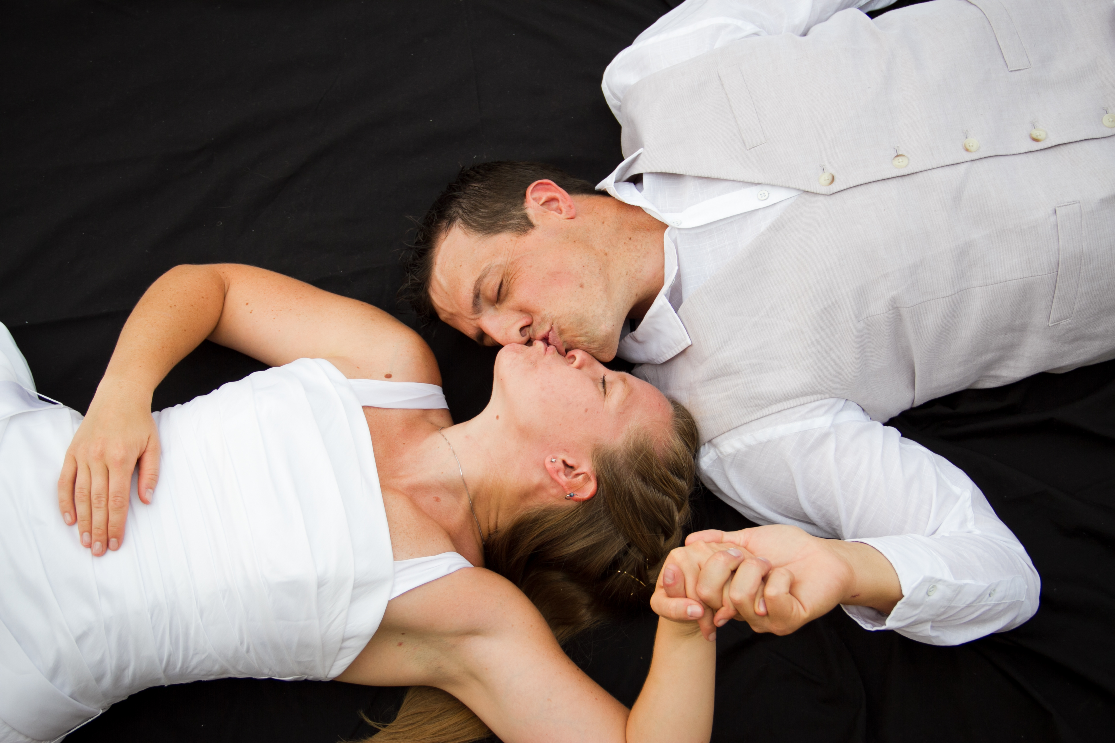 Bride and grooming kissing while laying on a black background.