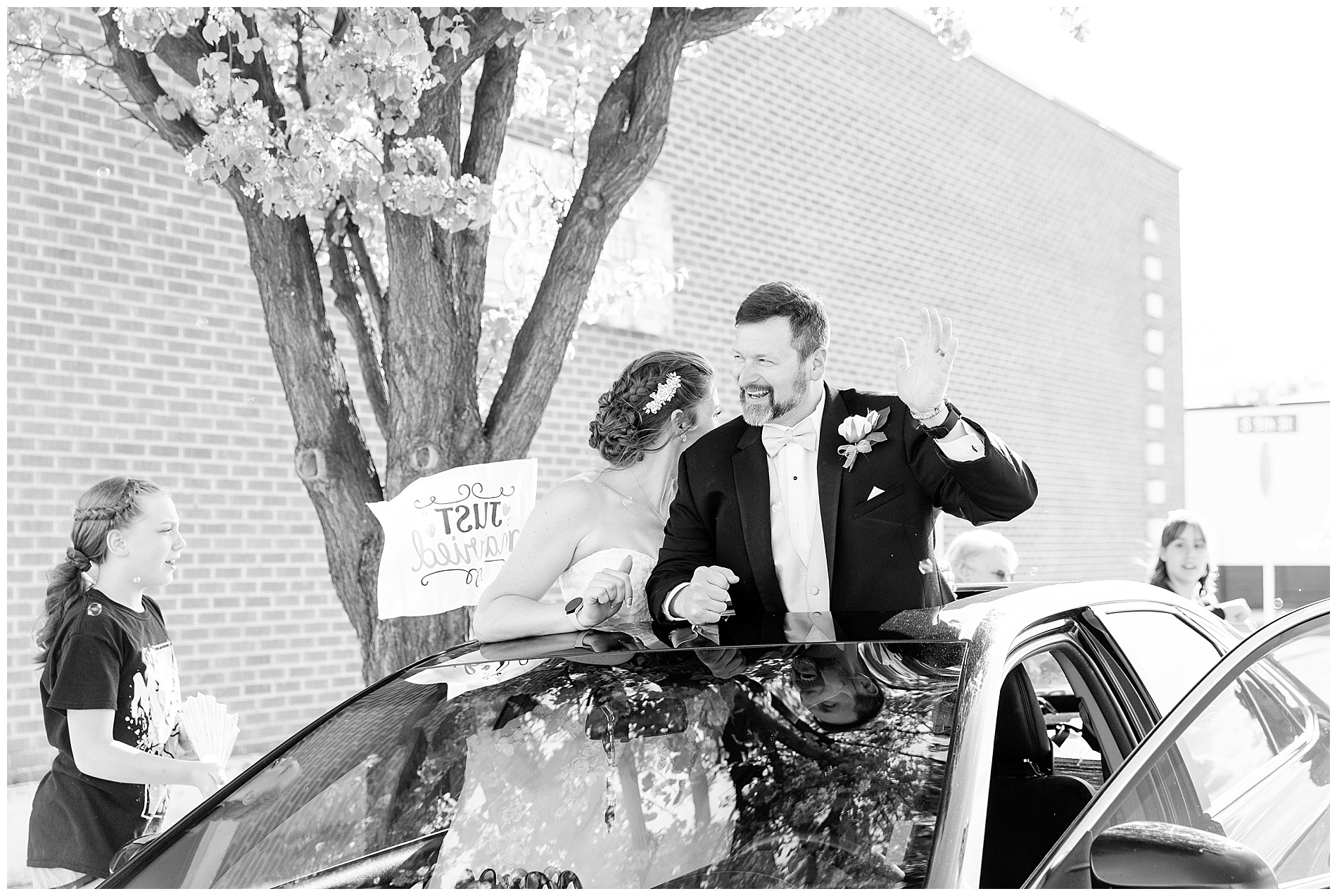 The groom waves through the sunroof of their getaway car