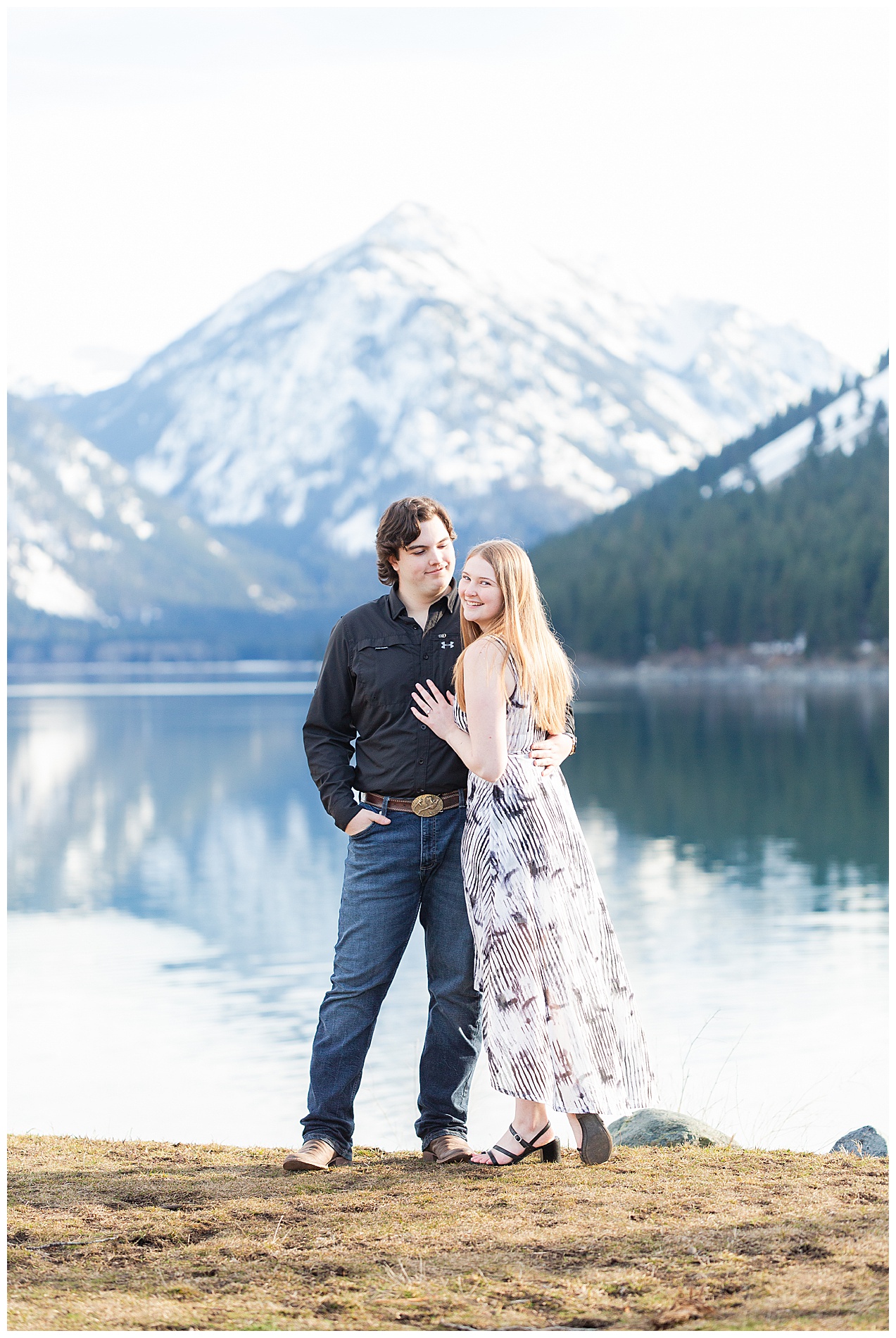 Engaged couple posing together with the snow-capped Wallowa Mountains and the lake in the background