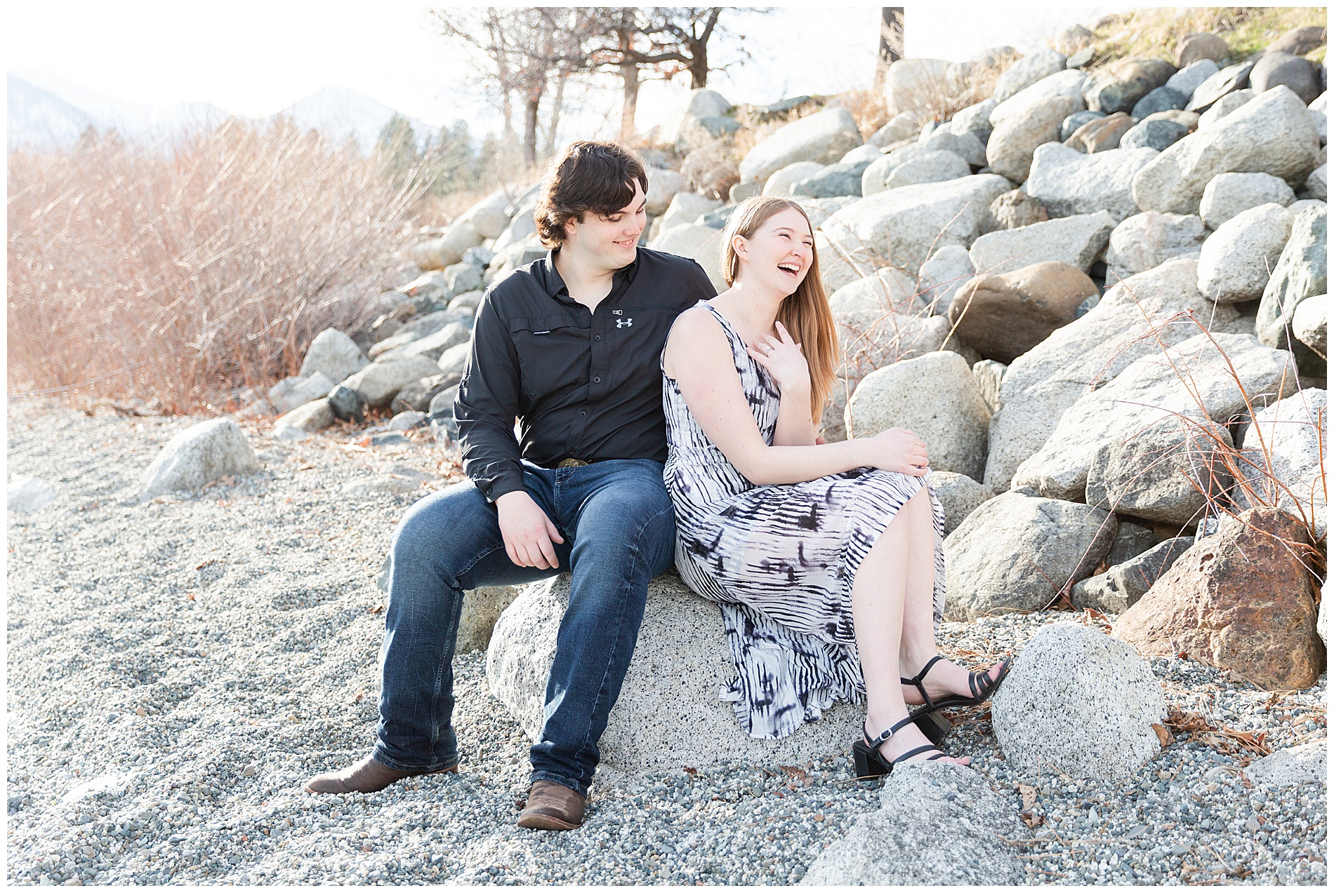 The groom-to-be making his fiancée laugh as they sit together on the rocks