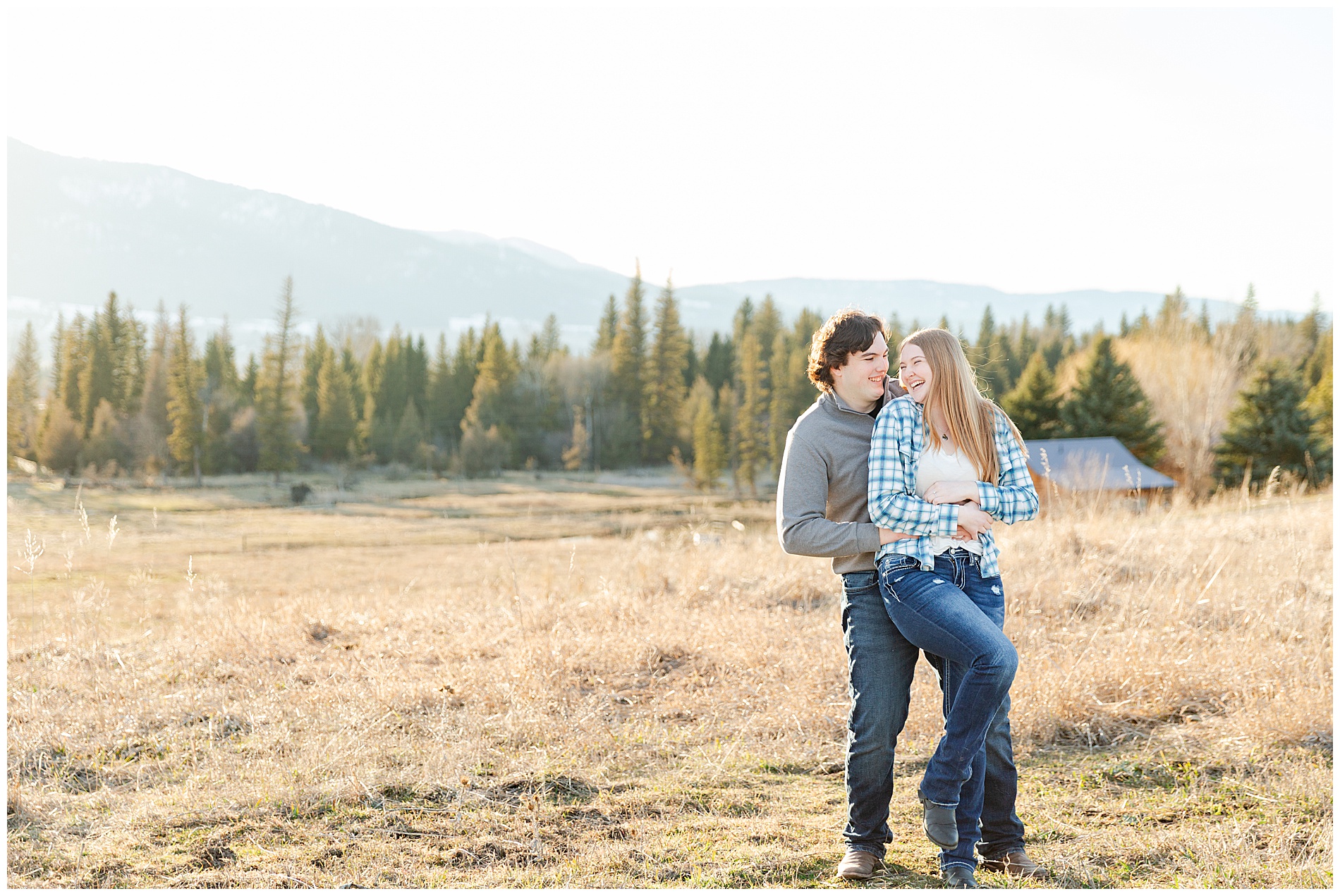 Engaged couple laughing with trees and mountains in the background