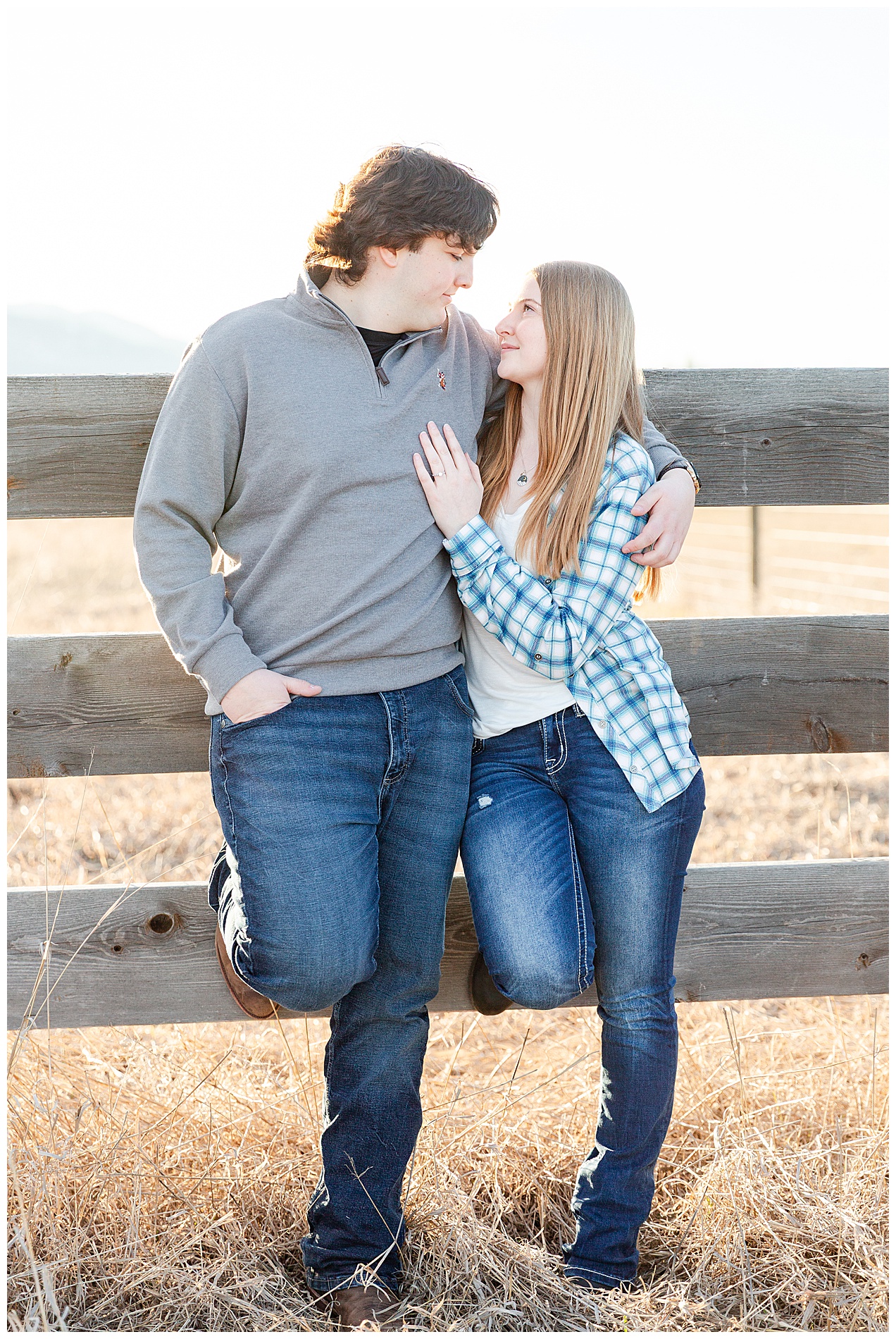 Engagement photo of a couple leaning against a wooden fence in eastern Oregon