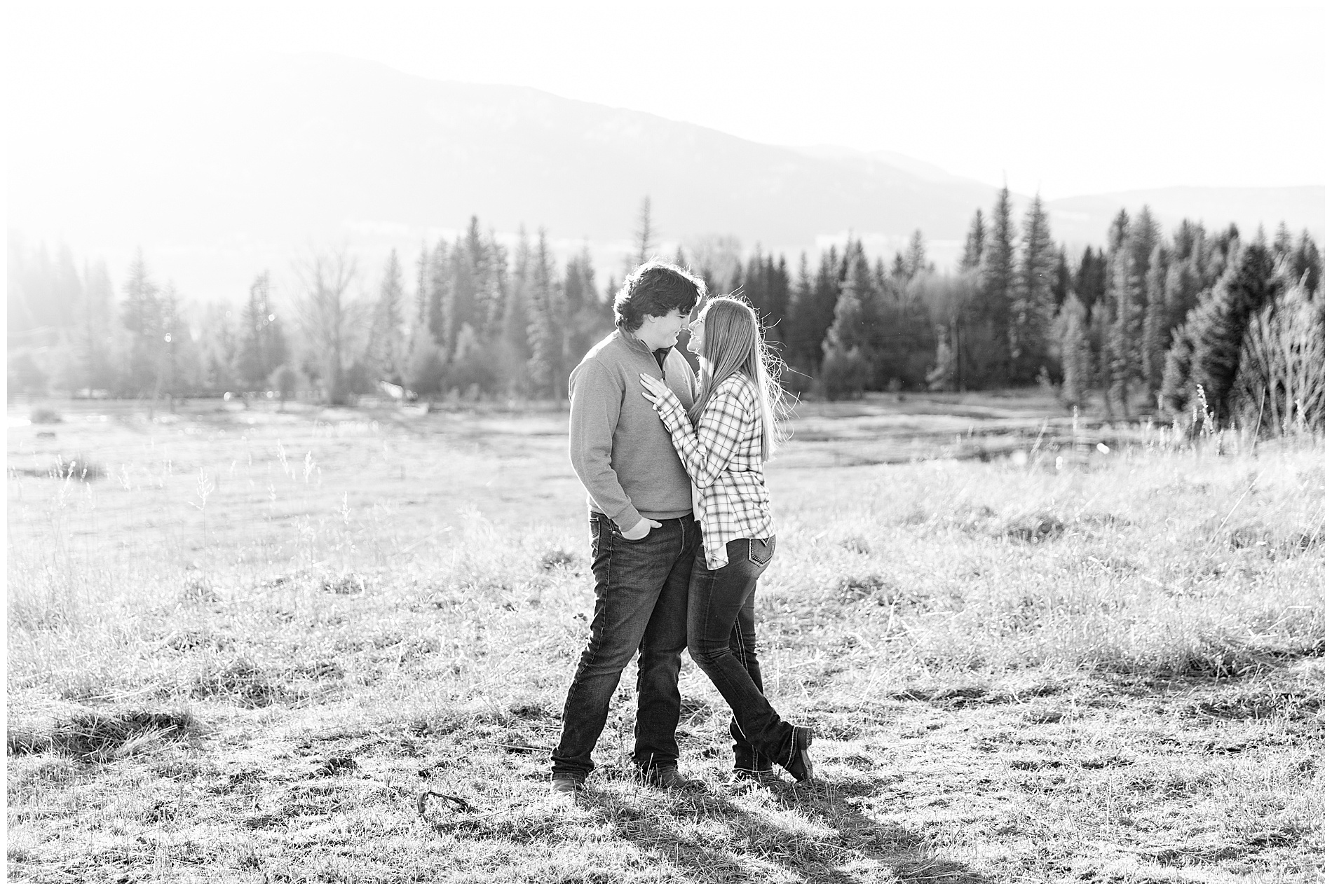 Engagement photo taken on a hill overlooking a conifer forest and a cabin