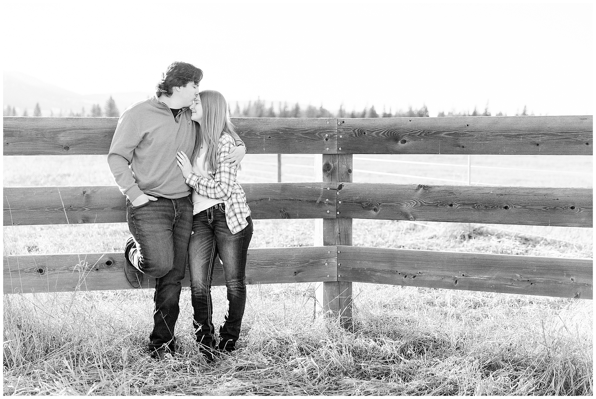 Engagement photo of a couple standing beside a wooden fence
