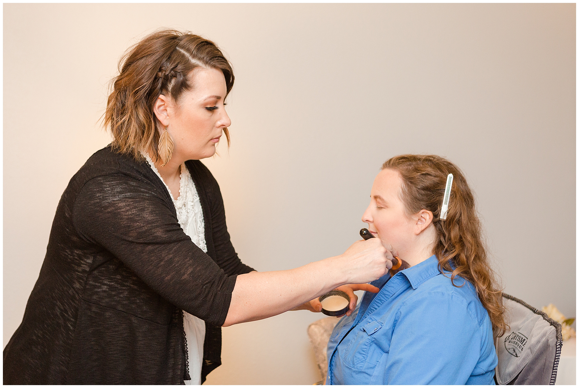 A makeup artists dusts the bride's face with powder