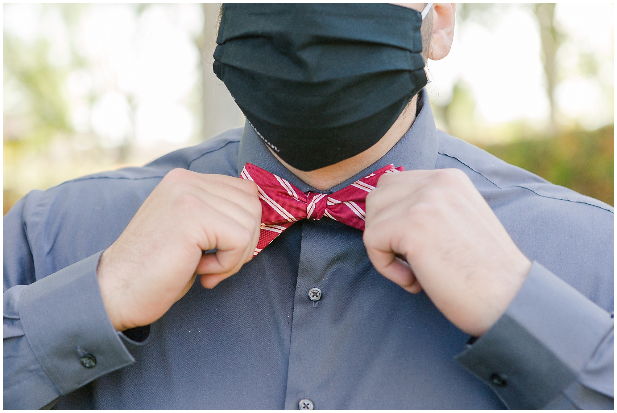 A groomsman in gray straightens his red striped bowtie