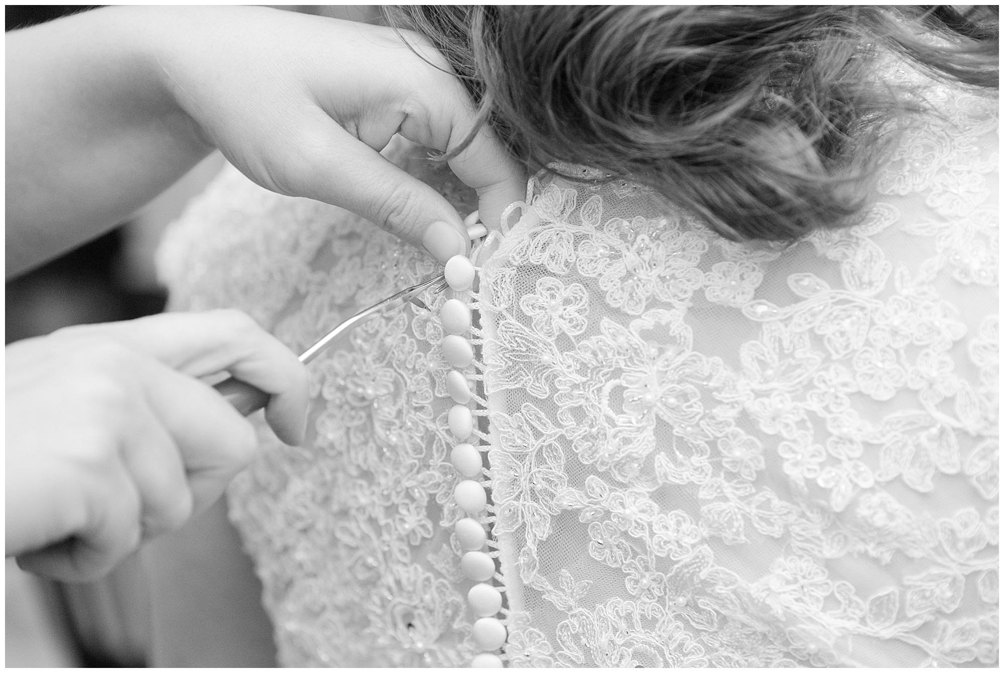 A bridesmaid's hands as she uses a crochet hook to button the bride's dress