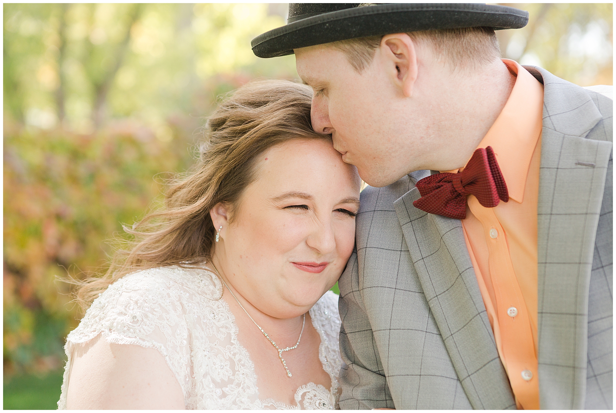 A groom in a top hat kisses his bride's forehead