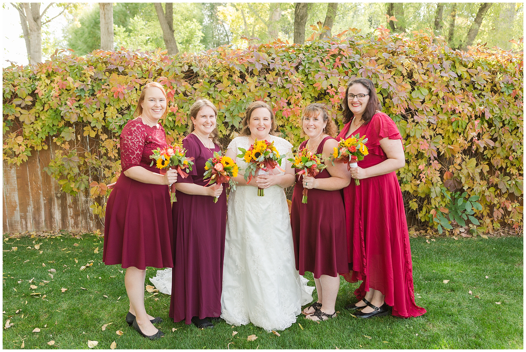 Bride and bridesmaids in front of a wooden fence covered in a vine that's changing into its fall colors