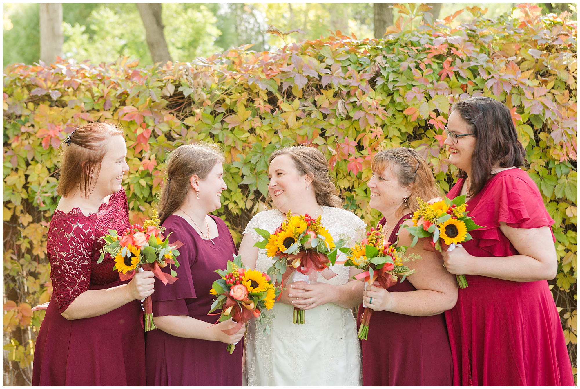 Autumn foliage behind the bride and bridesmaids, who are smiling at each other, in Nampa Idaho