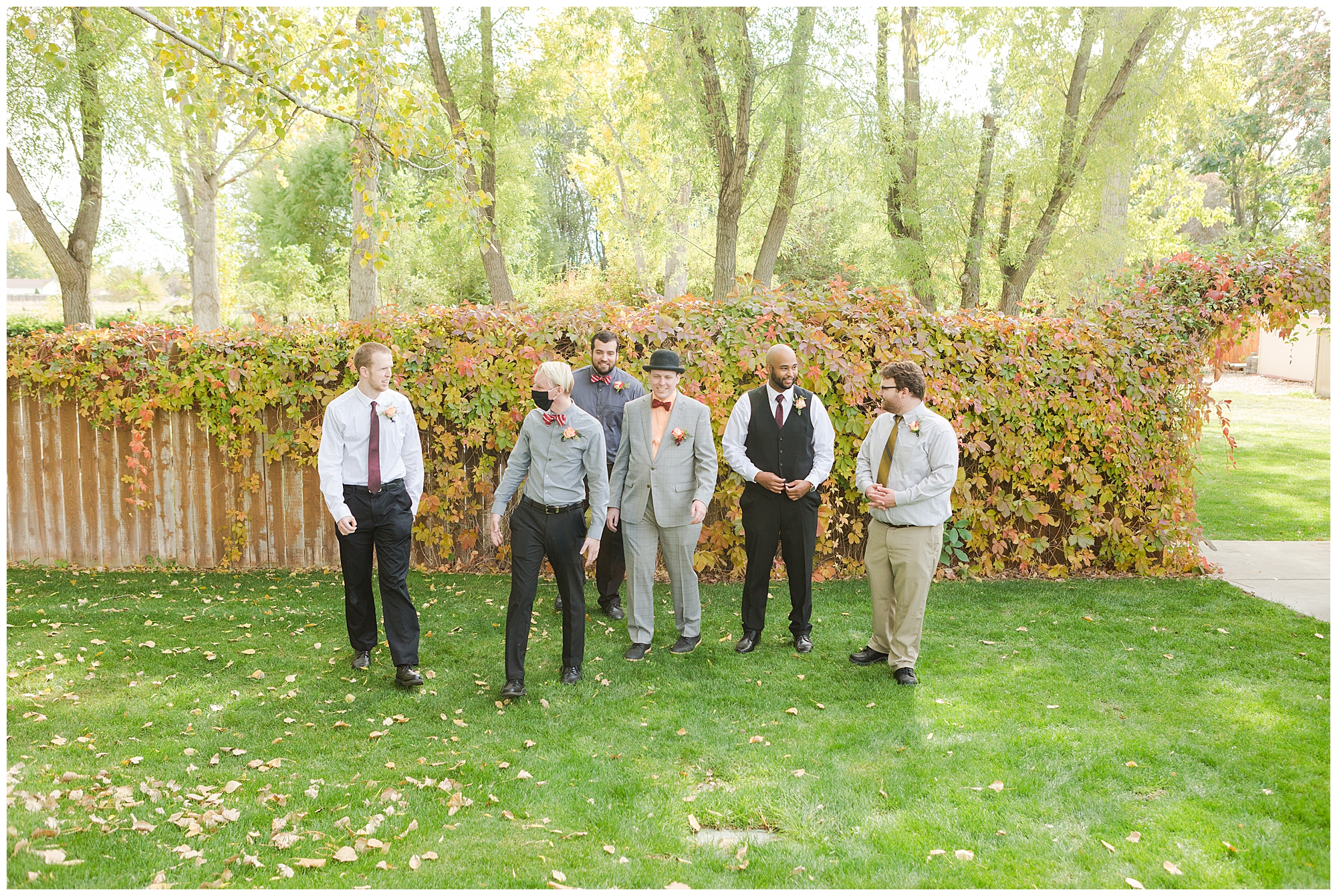 Groomsmen walk in front of a fence covered in a creeping vine that's changing into its autumn colors