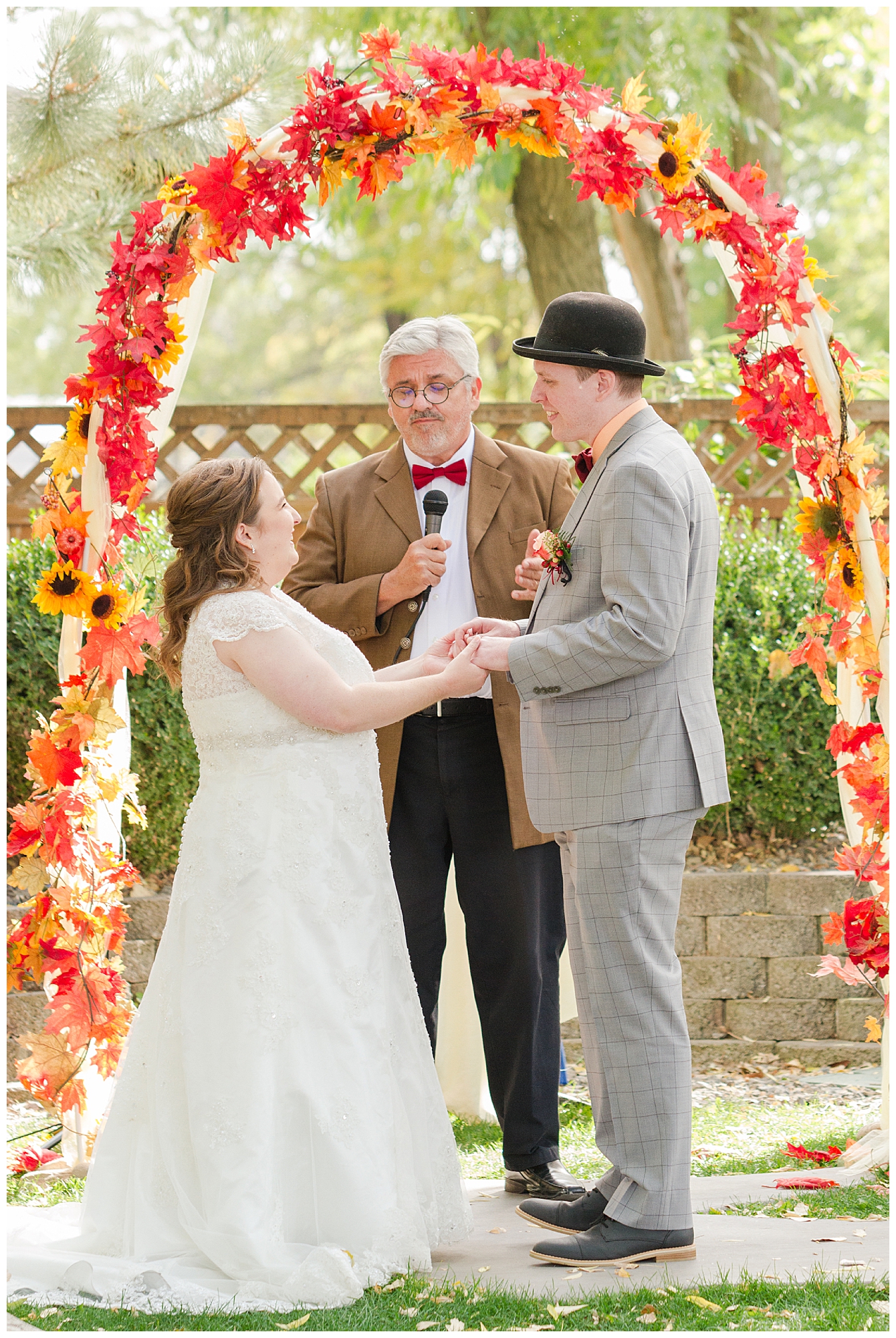 The bride and groom exchange vows under an arch decorated with autumn leaves and sunflowers