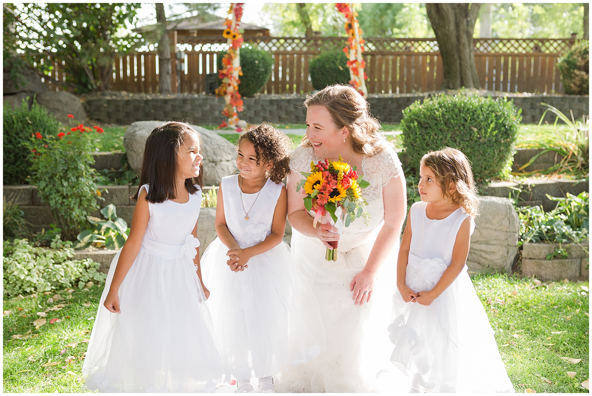 Three little flower girls in white with the bride--one girl is making a silly smile and one isn't sure what to think