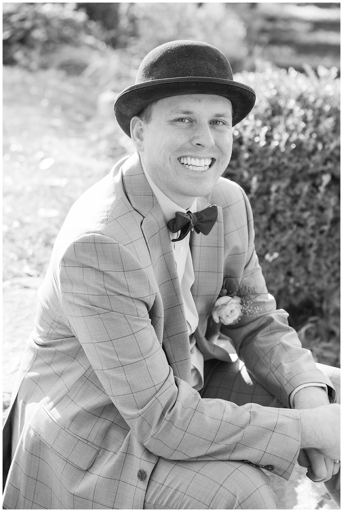 A black and white portrait of the smiling groom wearing a top hat