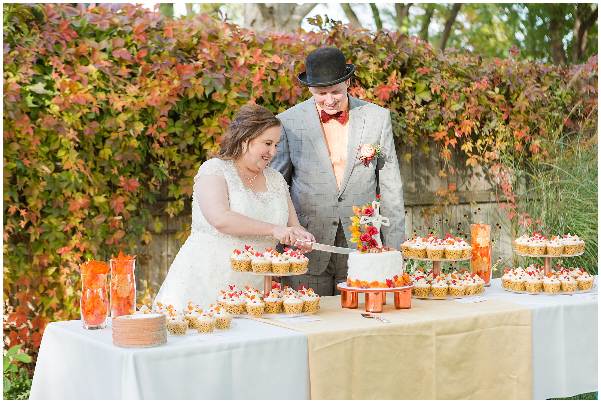 A bride cuts the autumn-themed wedding cake while the groom looks on, smiling