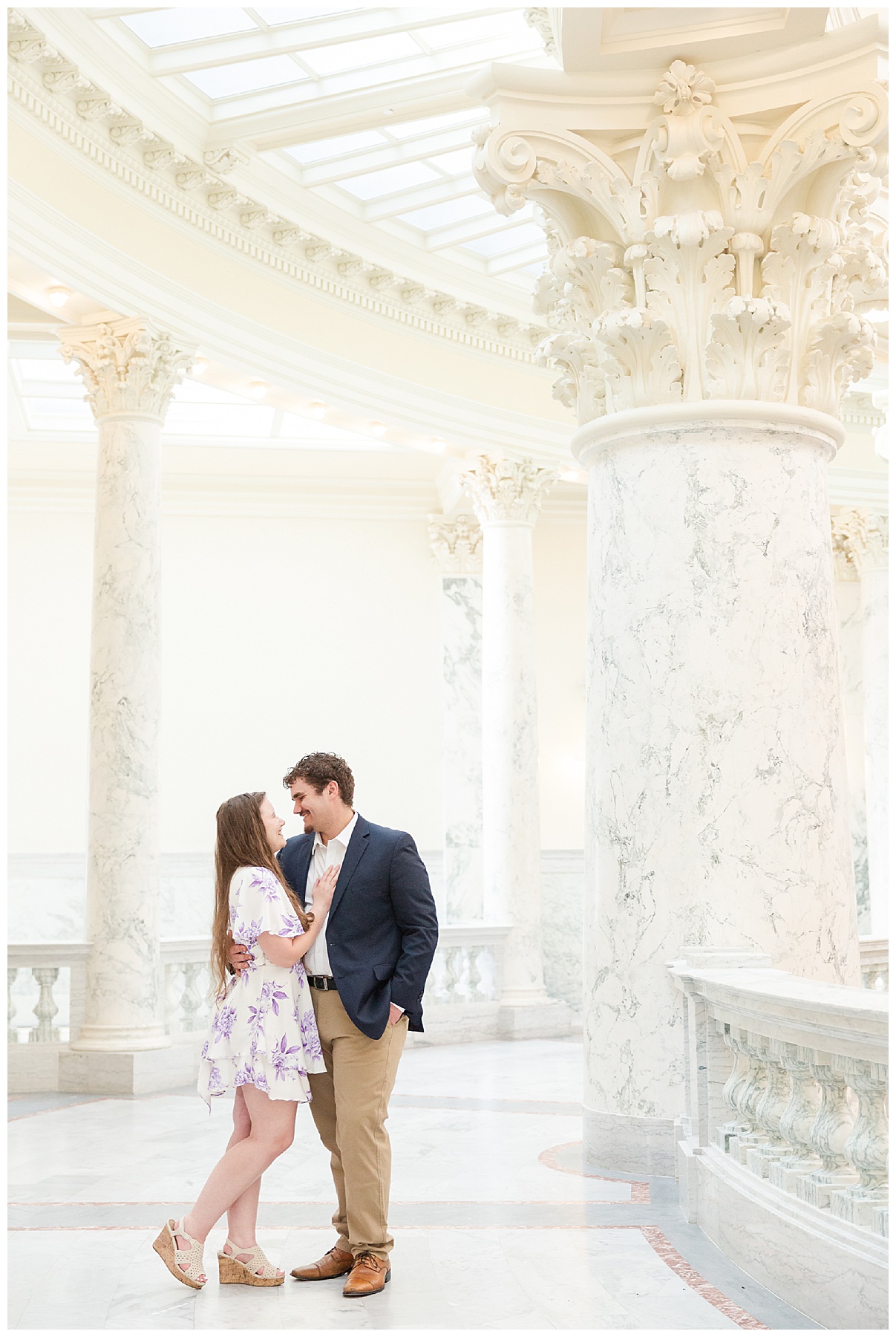 Engaged couple smiling at each other with large marble columns behind them