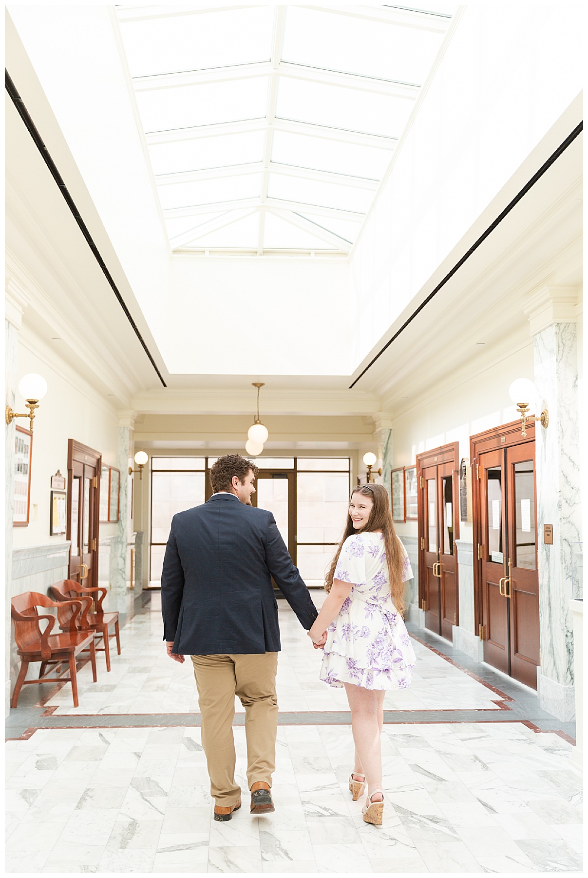 Engaged couple walking away down a hallway with the fiancée looking back over her shoulder and smiling toward the camera