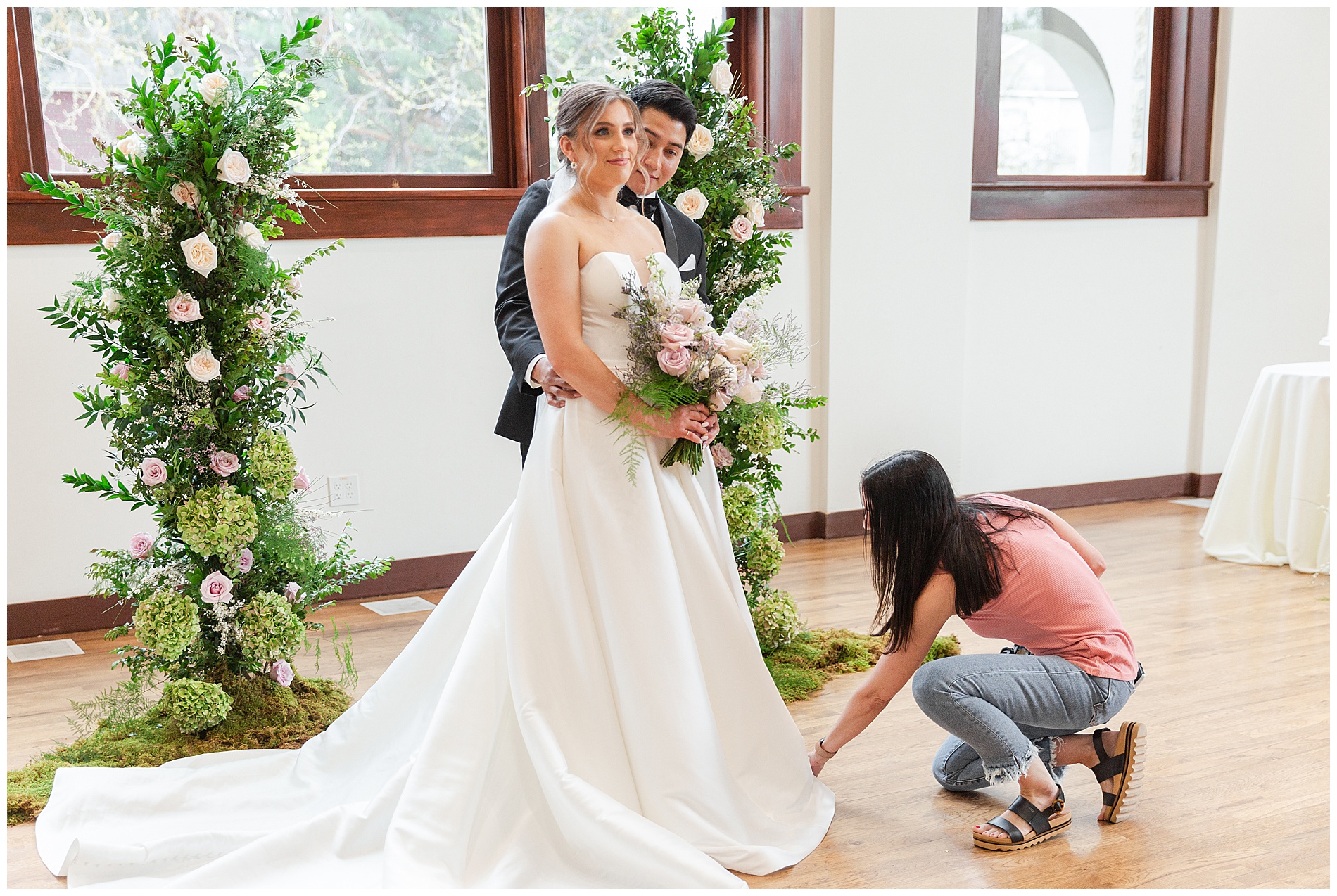 A photographer adjusts the bride's dress for photos