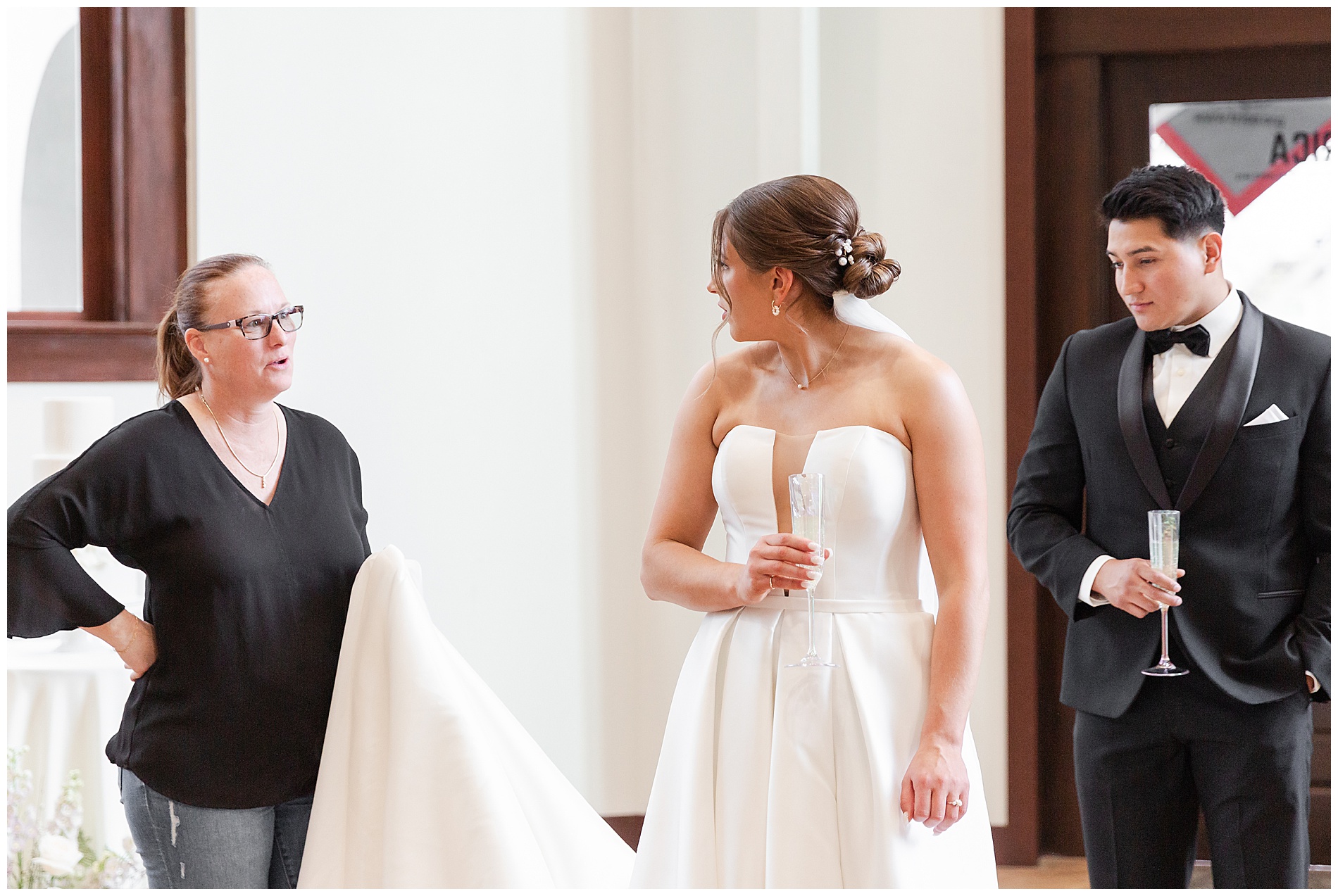The bridal shop owner holds the bride's train for her