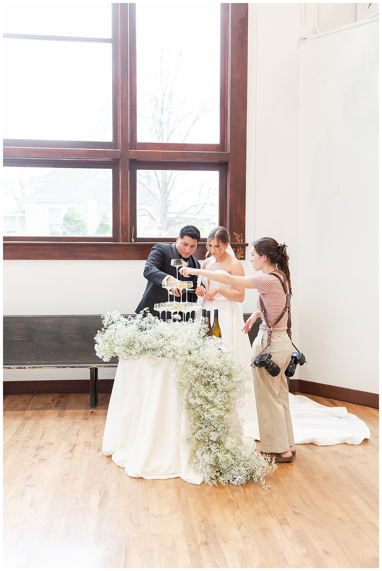 The photographer and event organizer helps the couple with pouring the champagne into the tower of glasses