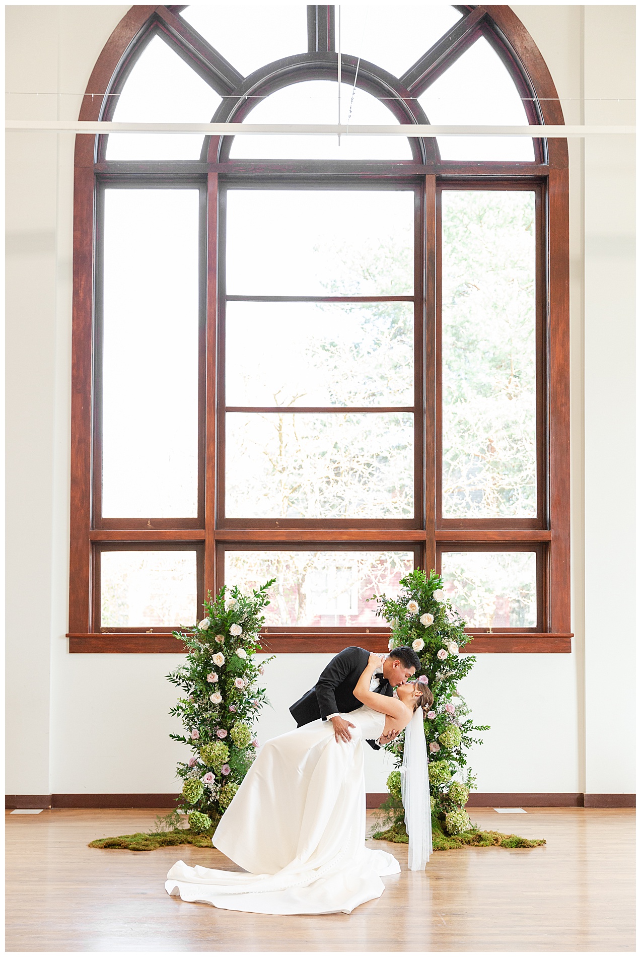 The big, beautiful windows of TRICA behind the couple as they kiss