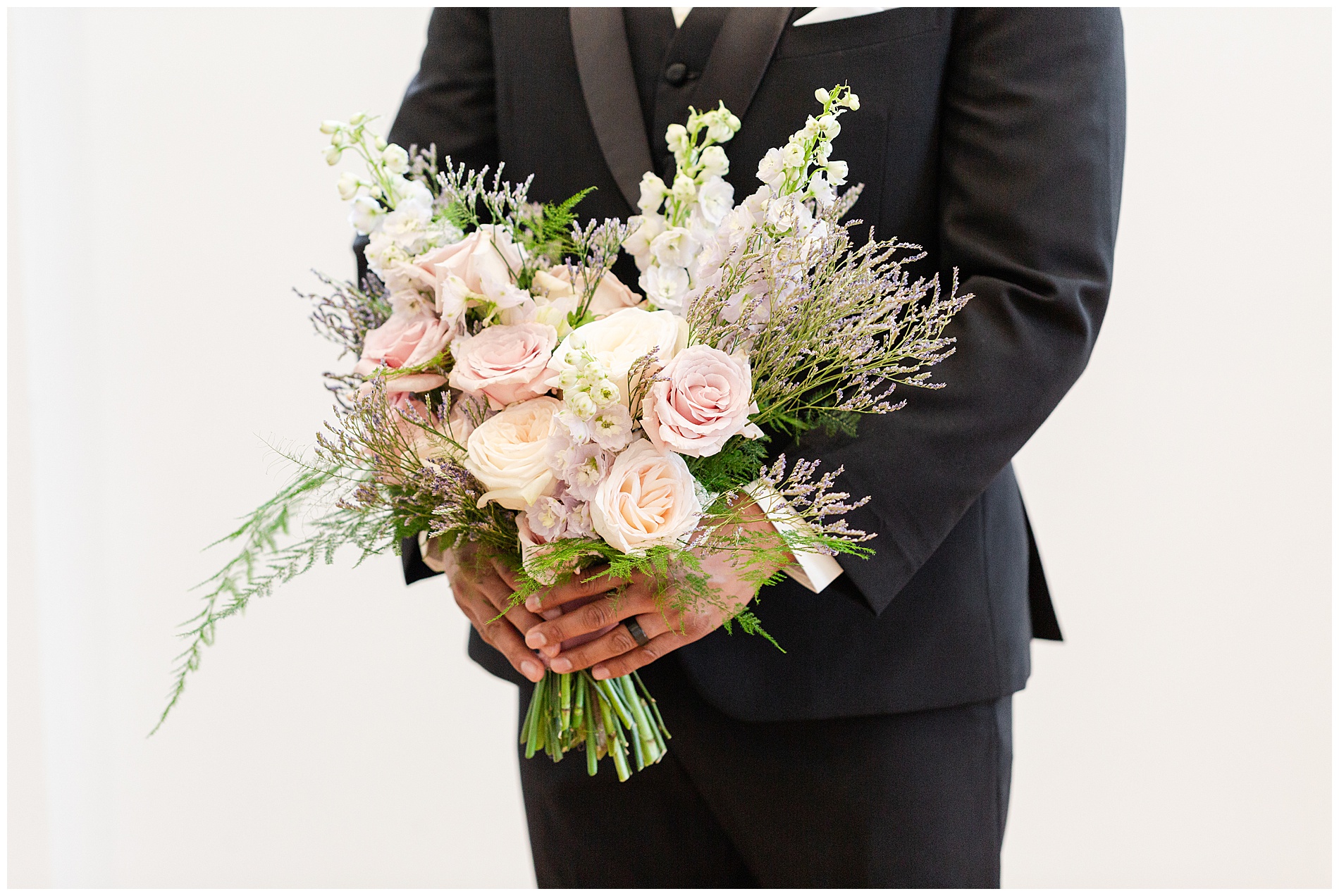 The groom's hands, holding the bride's bouquet for her