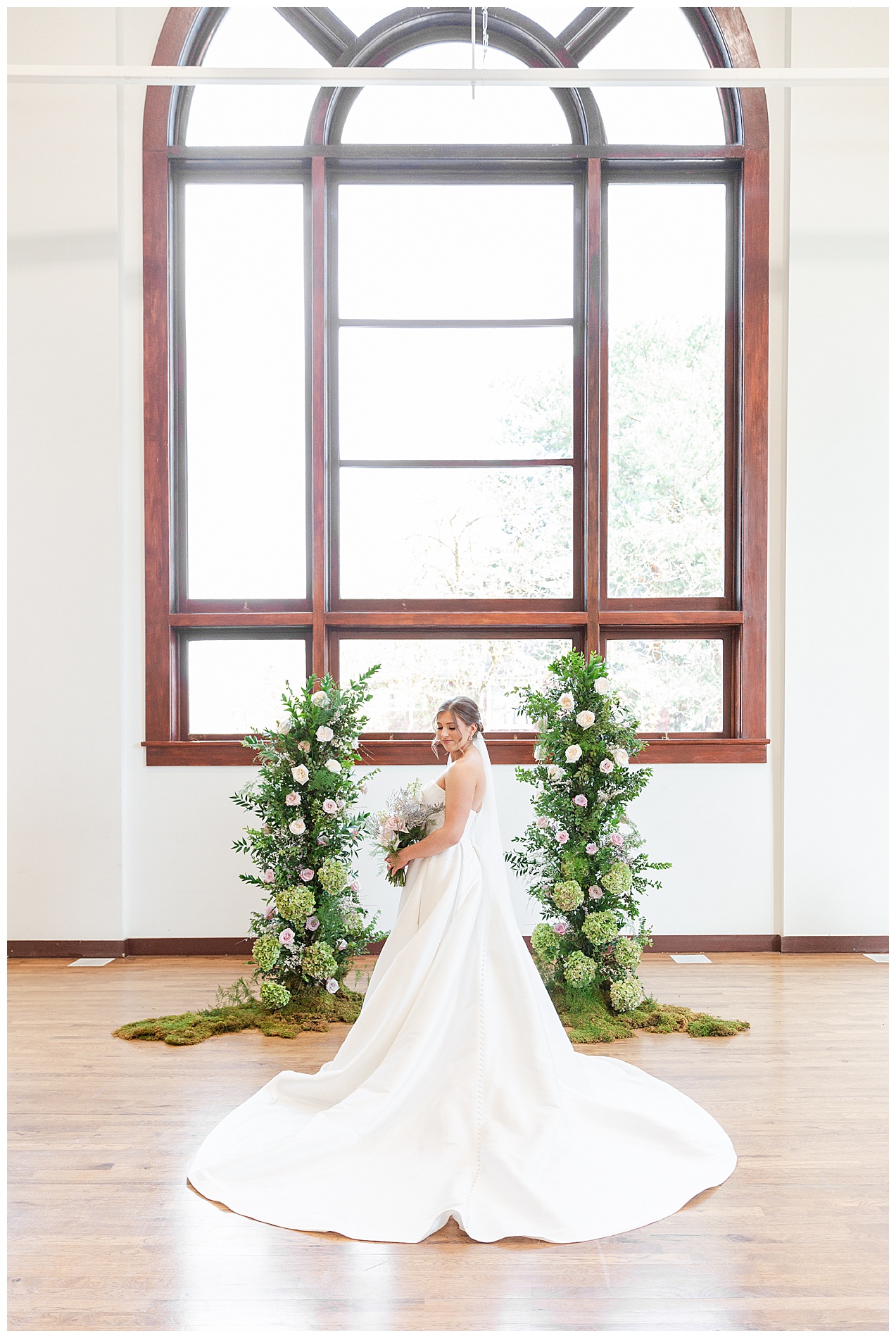Portrait of the bride's train spread out in front of the ceremony flowers and a large window