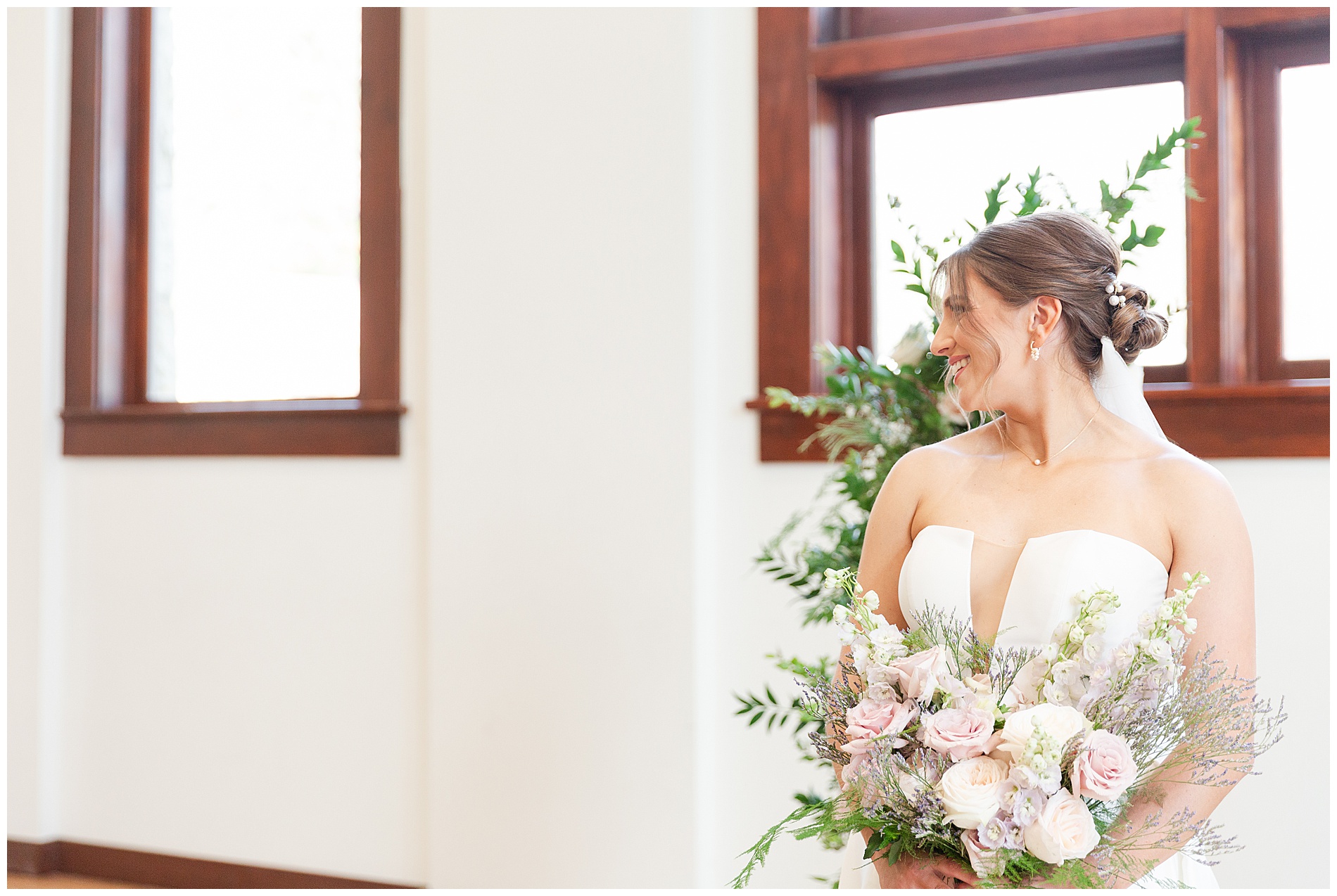 The bride smiles at the groom while he's having his portrait taken