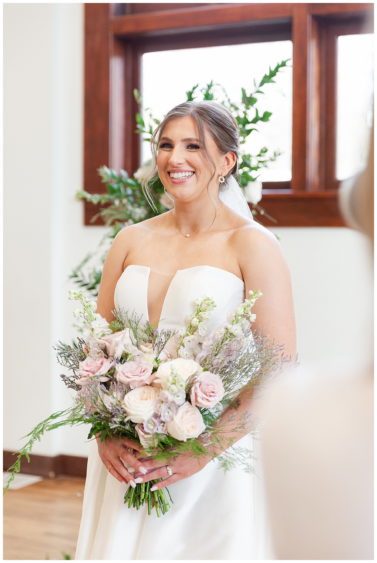 The bride smiles as a wedding photographer at the edge of the frame takes her photo