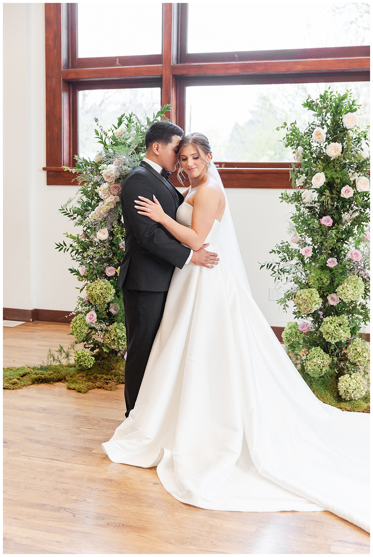 The bride and groom embrace in front of the large windows at TRICA