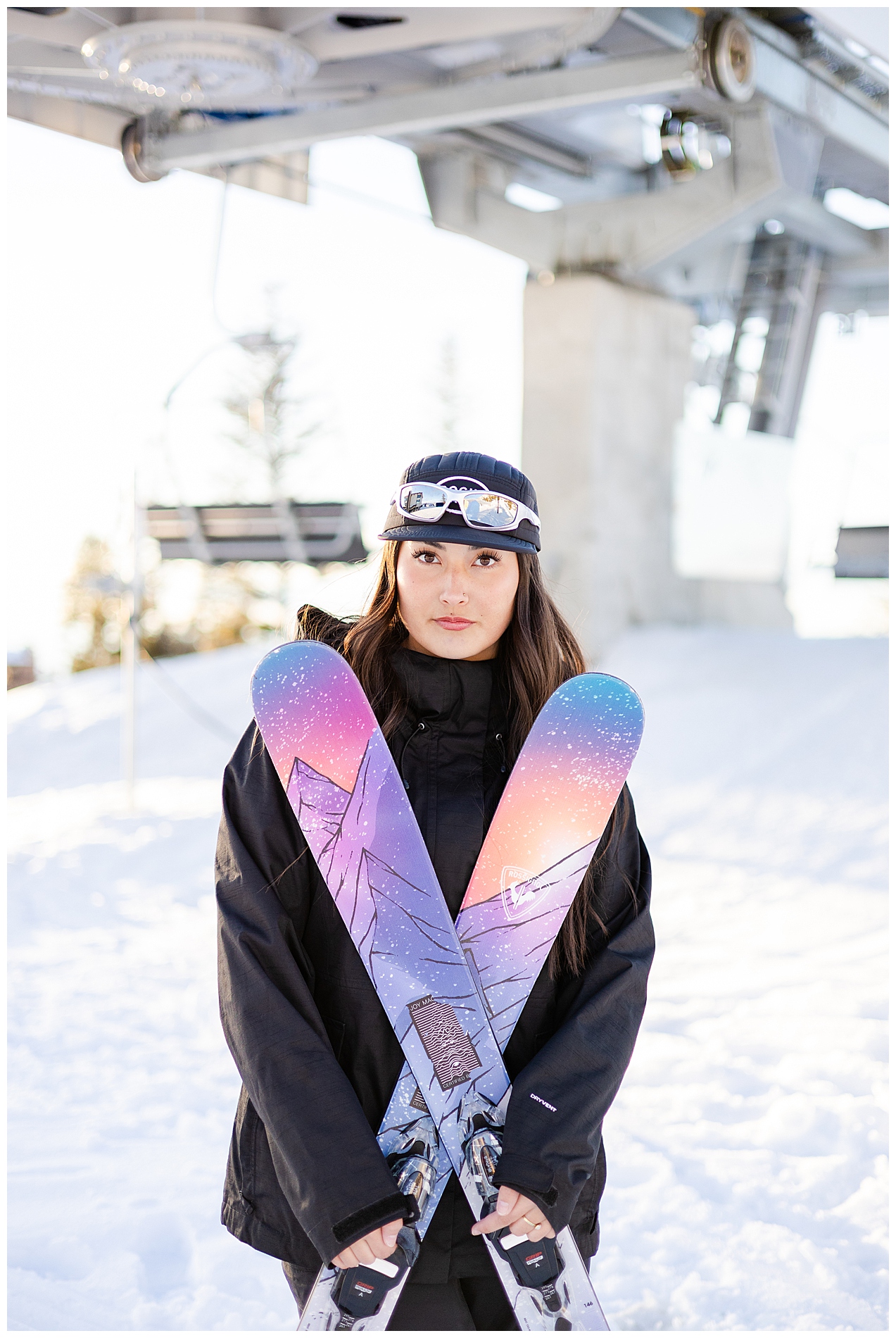Senior girl holds her skis in an X in front of a ski lift