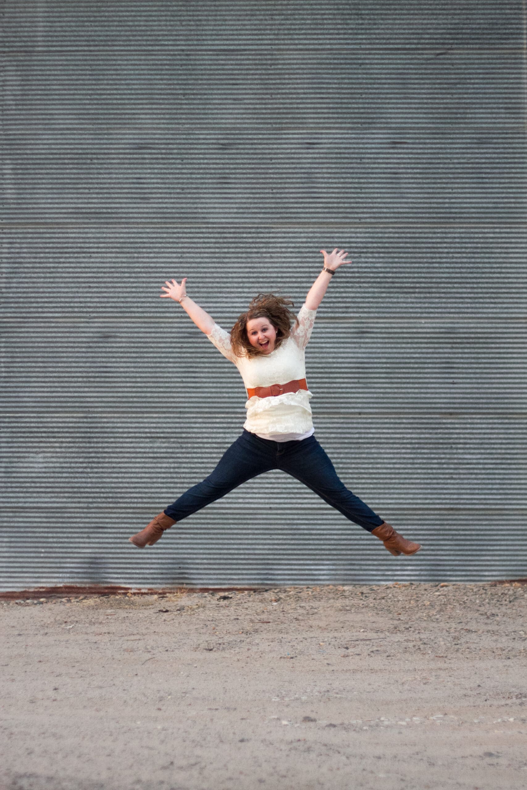 A girl jumps for joy in front of a corrugated metal building