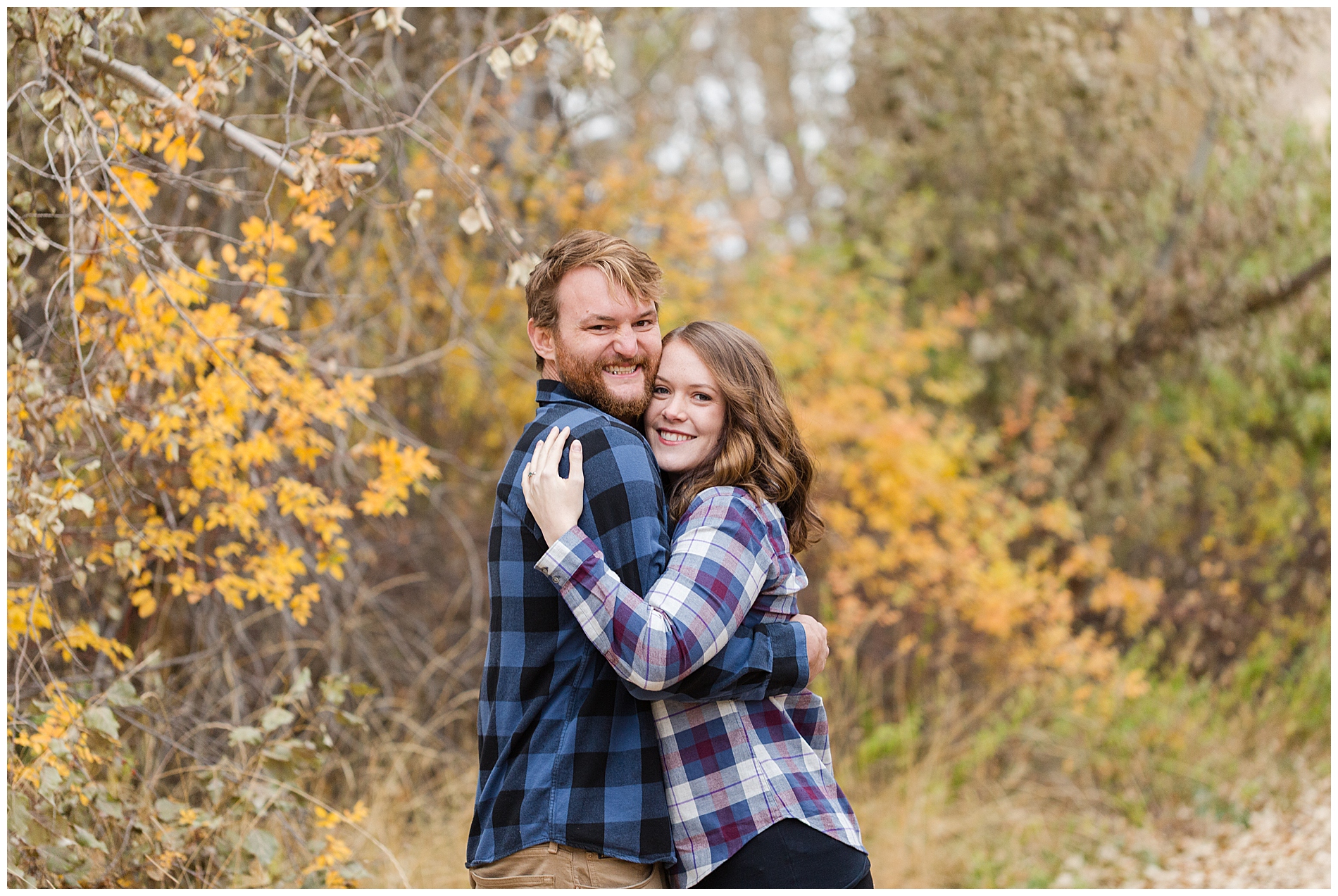 A couple in flannel hug with autumn leaves in the background