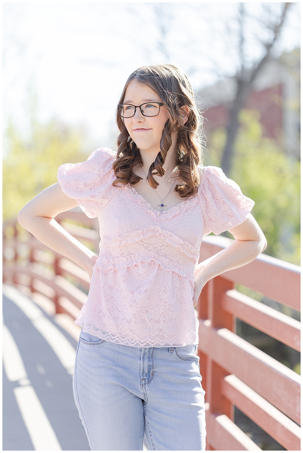 A high school senior girl in pink, standing on the bridge spanning from Julia Davis Park to the Boise State campus