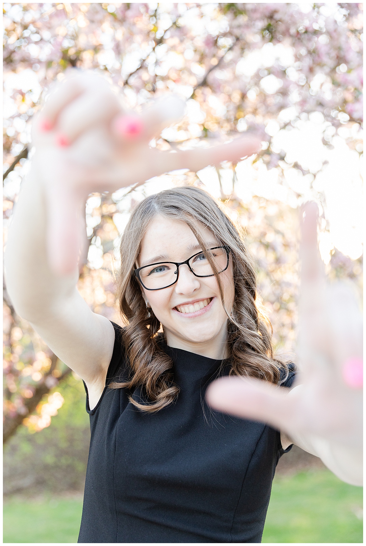 Senior girl holds her hands out toward the camera with a blossoming tree in the background