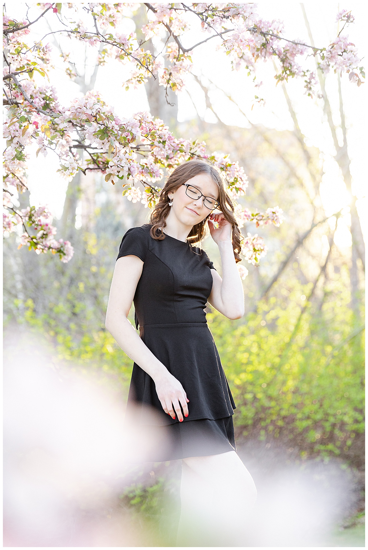 A girl brushes her hair behind her ear as the light shines through flowering trees